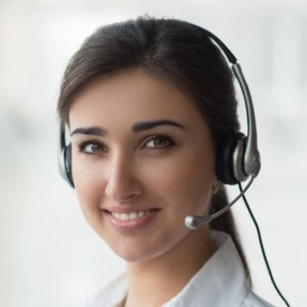 Okemos Dentist A young woman with dark hair, wearing a headset and microphone, smiles at the camera. She is dressed in a white shirt and appears to be in a bright, professional setting at an Okemos dental clinic.