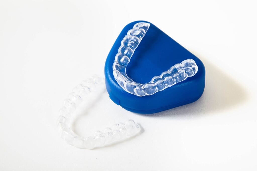 Okemos Dentist Two clear dental aligners, one placed on a closed blue plastic case and the other next to it, on a white surfaceโshowcasing care available at your local Okemos dentist.